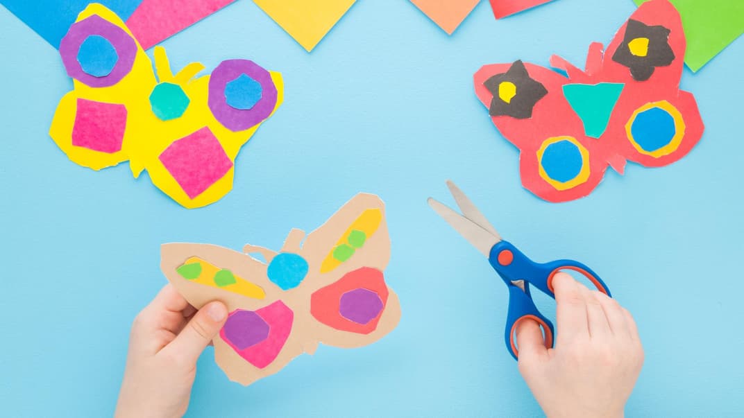 Ein Kind bastelt Schmetterlinge und hält eine Schere in der Hand.