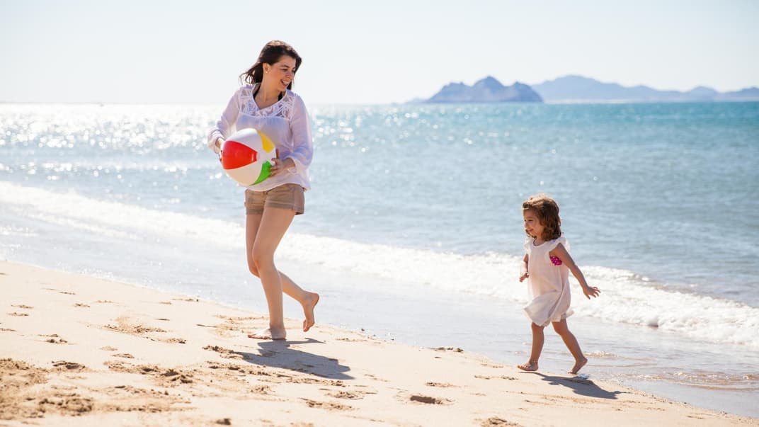 Junge Frau spielt mit Kind am Strand.