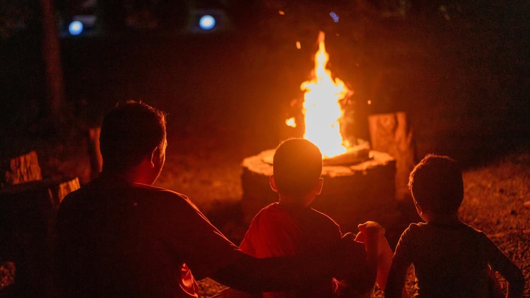 Ein Vater sitzt mit seinen beiden Kindern am Lagerfeuer. 