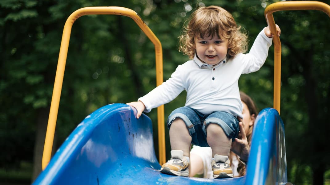 Ein kleines Kind traut sich nicht alleine zu rutschen. 