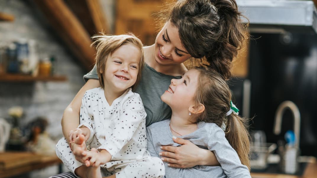 Mama hält ihre zwei Kindern im Arm.