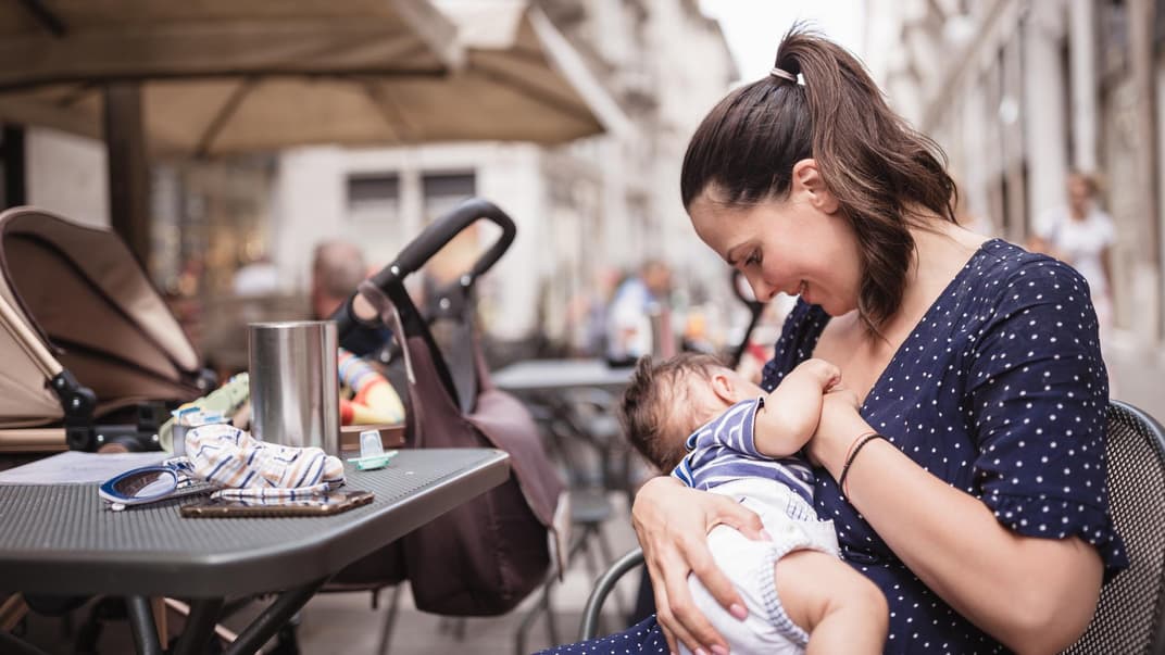 Eine Mutter stillt ihr Baby draußen in einem Café.