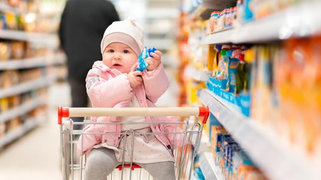 Ein kleines Baby hat in einem Supermarkt einen Quetschie in der Hand. 