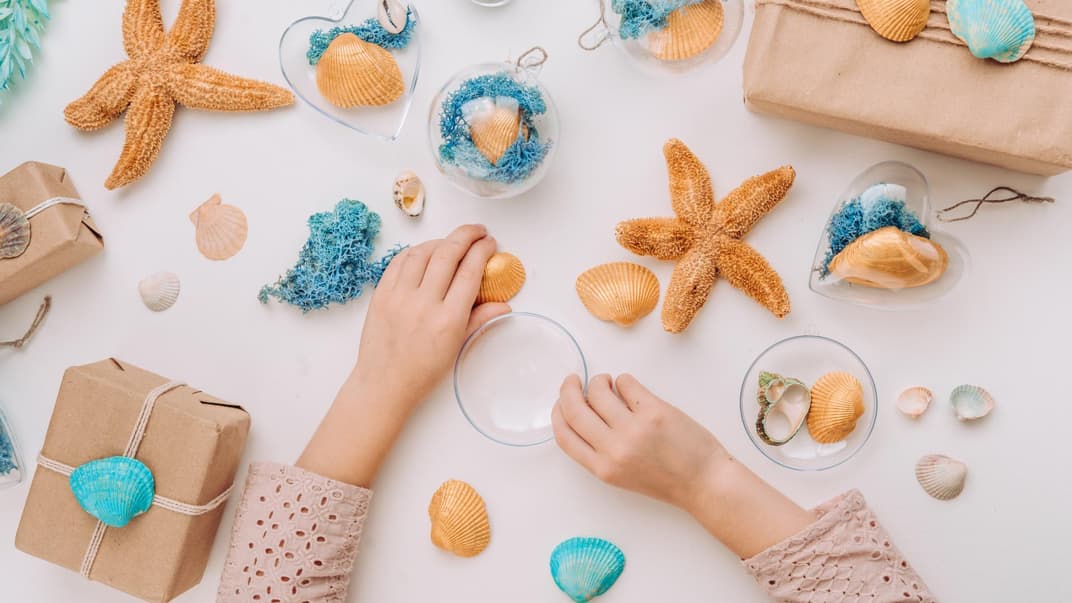 Kind basteln am Tisch mit Muscheln und Seesternen.