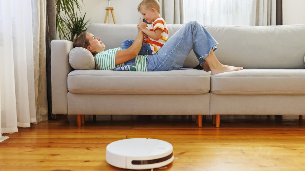 Mutter und Kind sitzen auf dem Sofa vor einem Saug-Roboter.