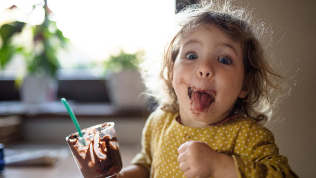 Kleines Kind mit Schoko-Dessert streckt die Zunge raus.