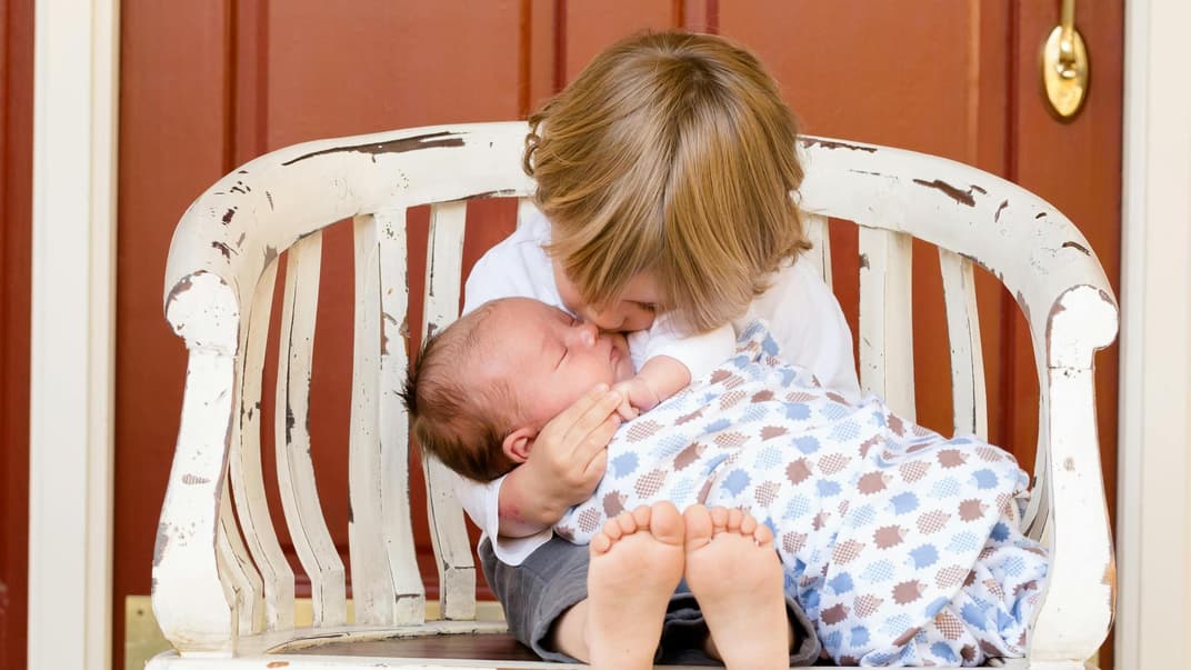 Ein kleiner Junge küsst seine Baby-Schwester, die er im Arm hält. 