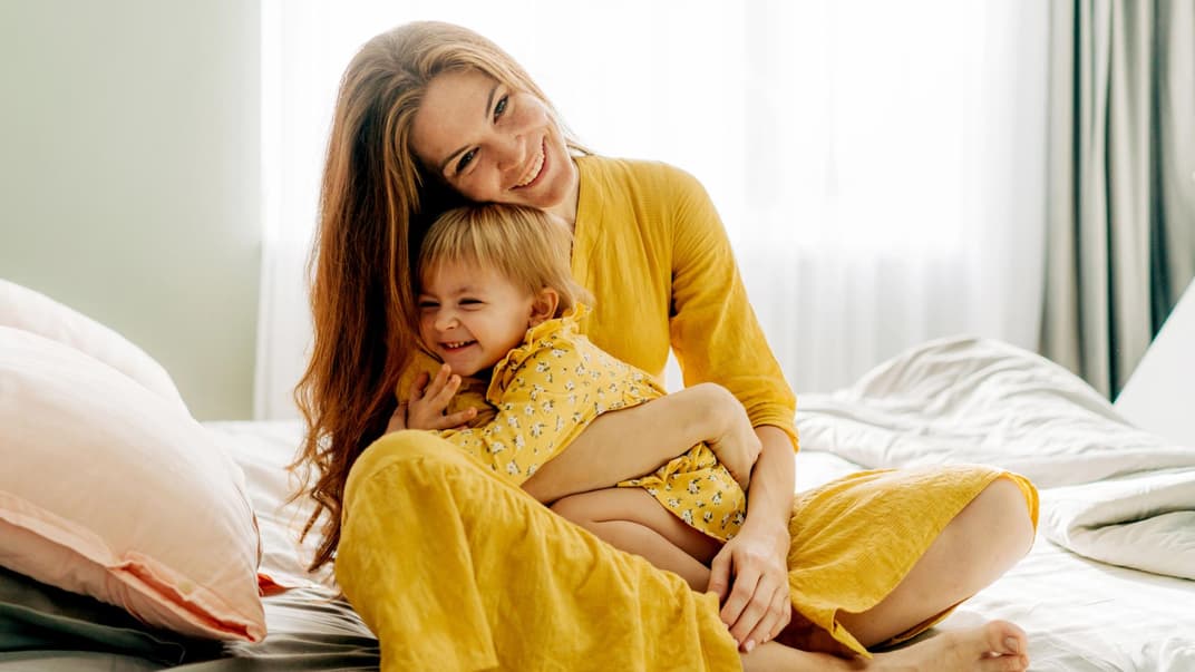 Mama und Kind umarmen sich auf dem Bett.