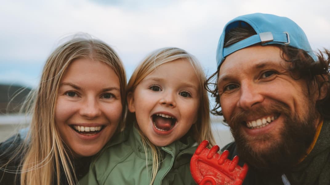 Mama, Papa und Kind lachen in die Kamera.
