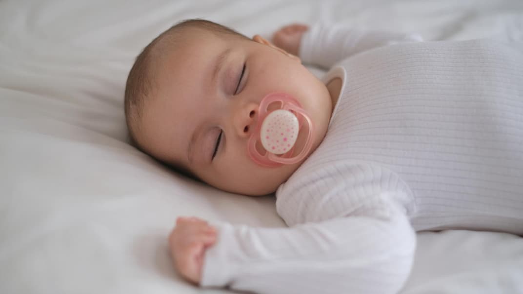 Schlafendes Baby mit Schnuller im Bett