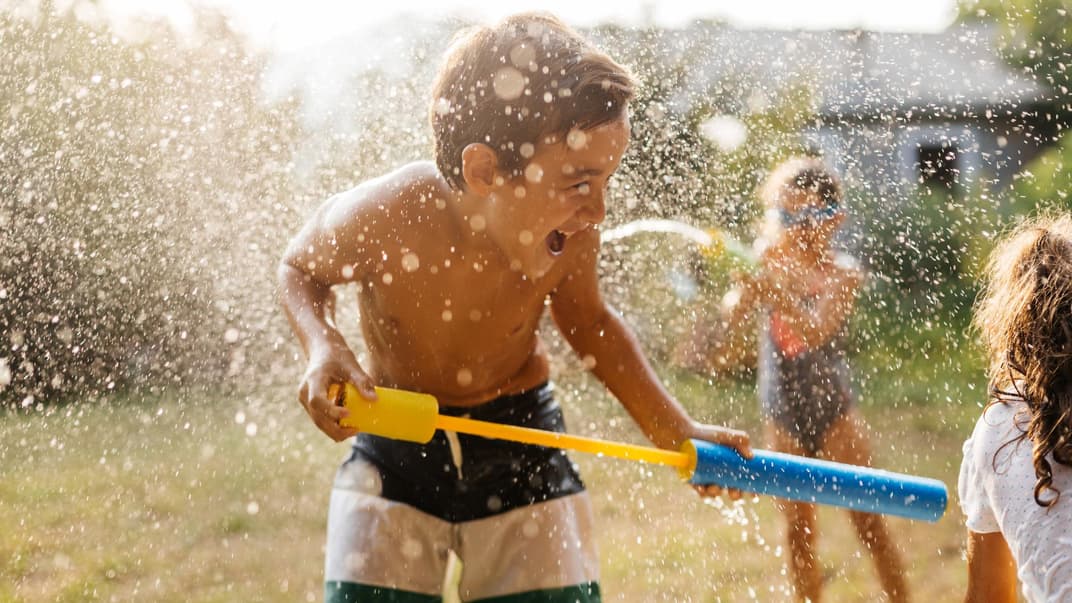 Junge spielt im Garten mit Wasserpistole.