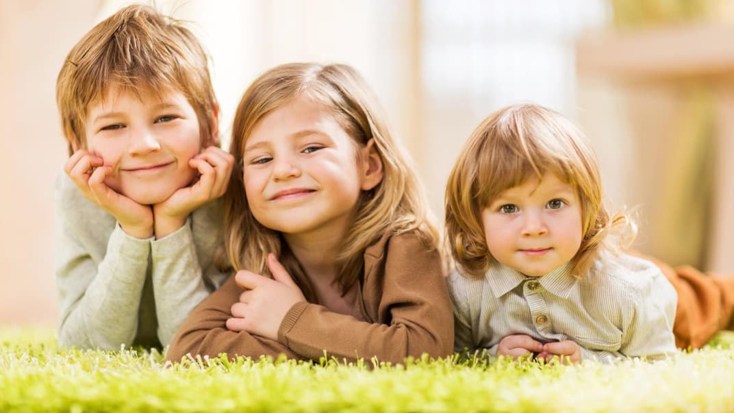 Drei Kinder liegen auf dem Teppich.