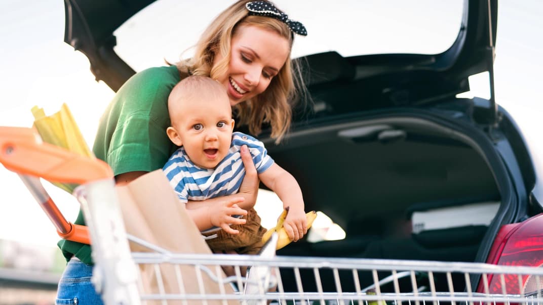 Mutter mit Baby und Einkaufswagen am Auto