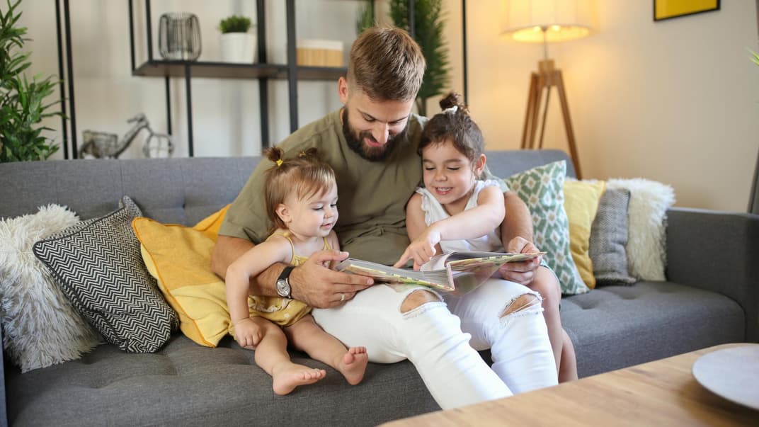 Kinder lieben es, Bilder "von früher" zu sehen. Vater schaut sich mit zwei Kindern Fotoalbum an.