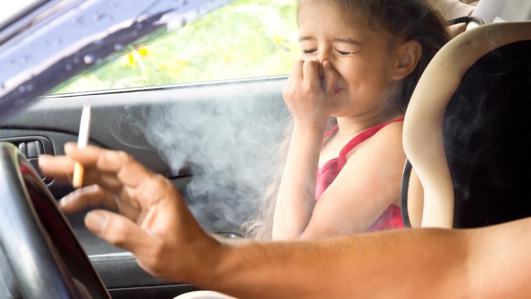 Kind hält sich wegen Zigarrettenrauch im Auto die Nase zu.