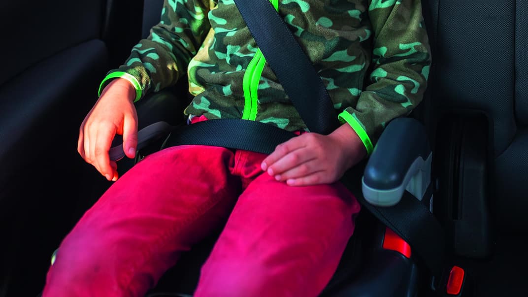 Eine Junge sitzt im Auto auf einer Sitzerhöhung. 