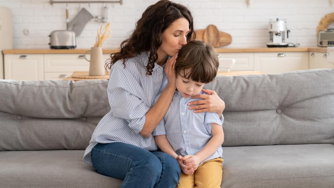 Mutter umarmt Sohn auf dem Sofa.