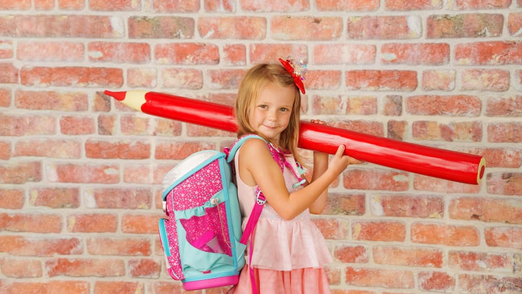 Kind mit Schulranzen und riesigem Buntstift.