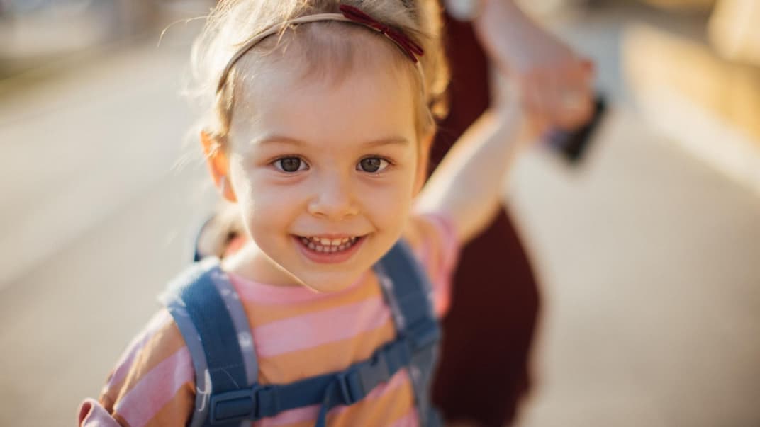 Mädchen mit Kita-Rucksack an der Hand ihrer Mama