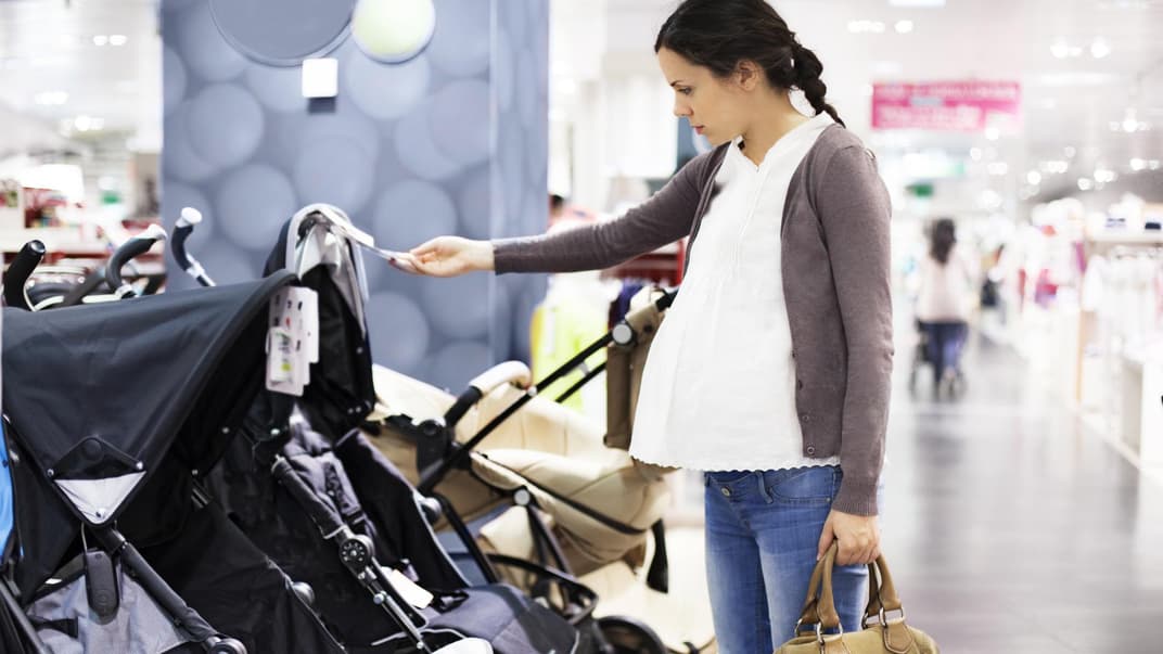 Eine Mutter mit Babybauch steht im Geschäft und schaut sich Kinderwagen an. 