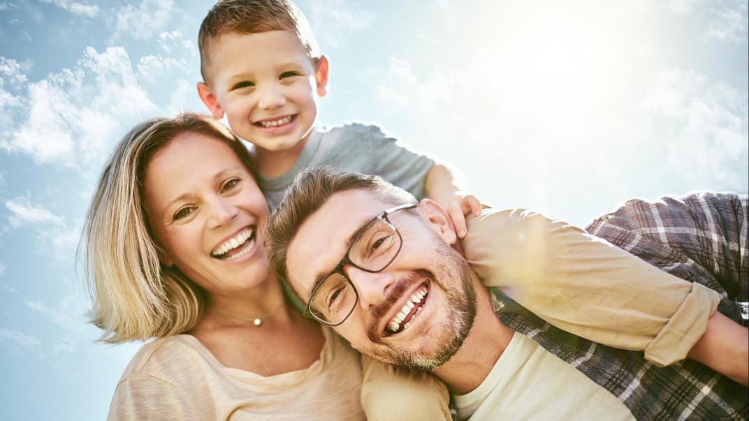 Eltern mit Kind lachen in die Kamera.