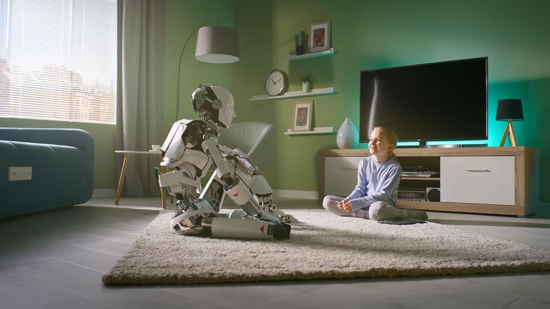 Kind sitzt mit einem Roboter im Wohnzimmer. 