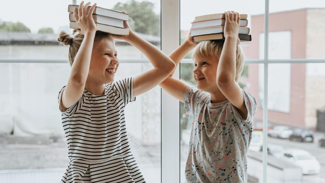 Fröhliche Kinder mit Büchern auf dem Kopf.