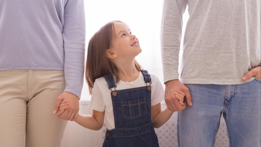 Lächelndes Mädchen steht zwischen ihren Eltern.