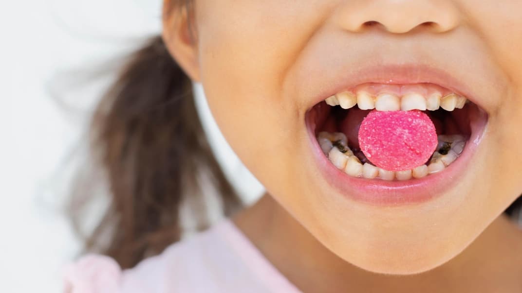 Ein Mädchen mit Bonbon zwischen den Zähnen. 