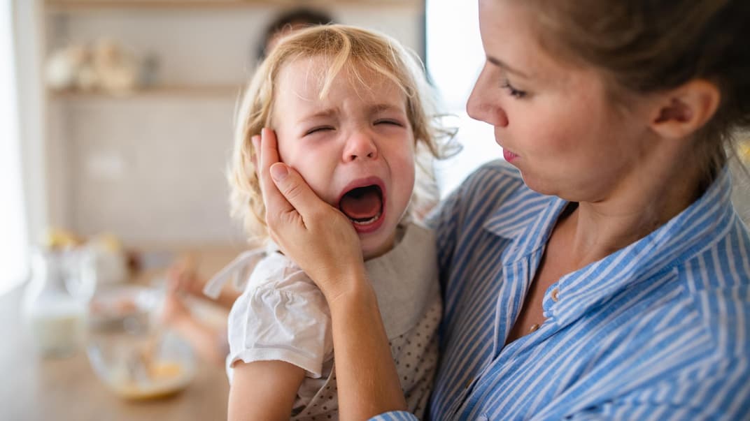 Mutter hält weinendes Kleinkind auf dem Arm.