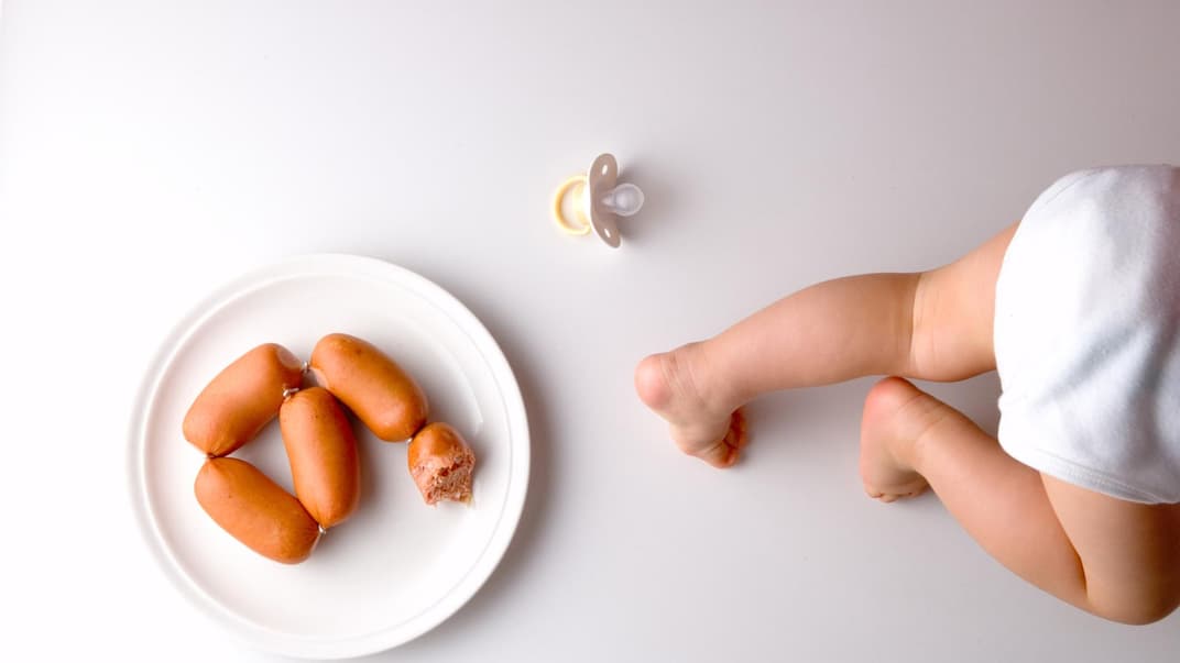 Baby krabbelt weg von einem Würstchenteller.