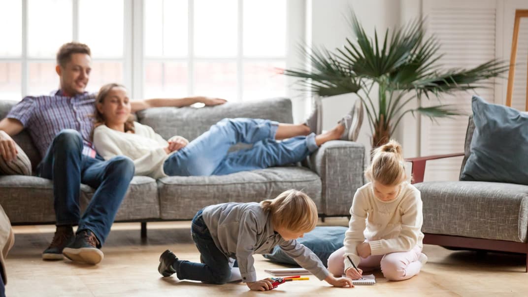 Eltern sitzen auf dem Sofa, Kinder spielen.