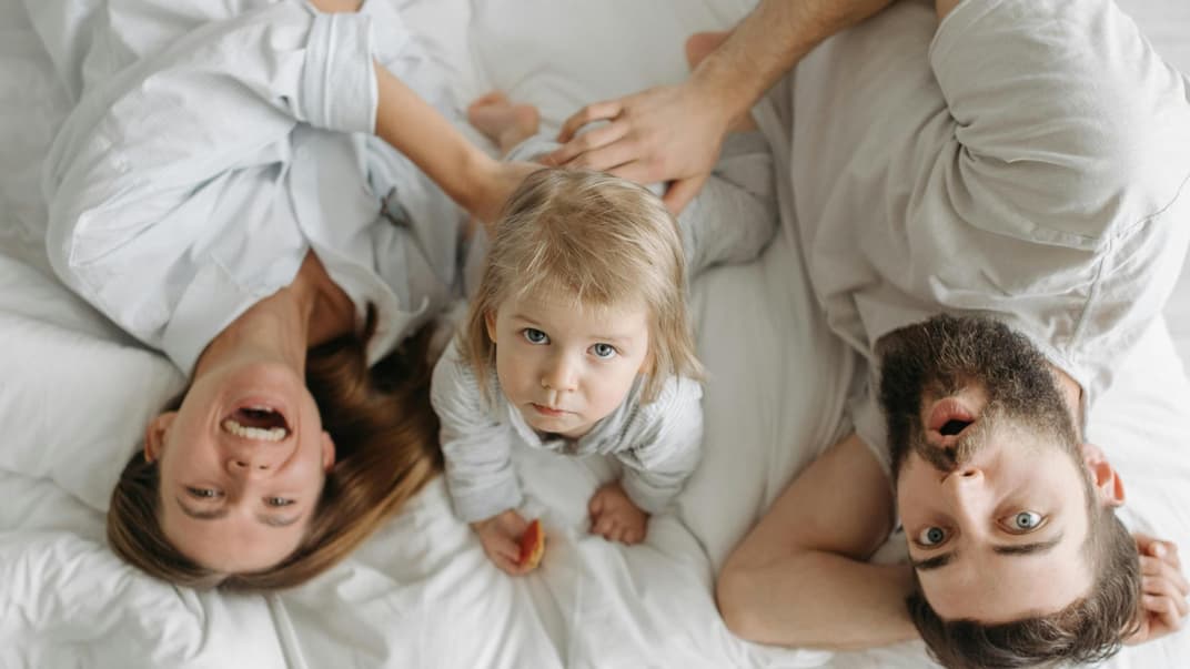 Eltern liegen mit Baby auf dem Bett und machen Quatsch.