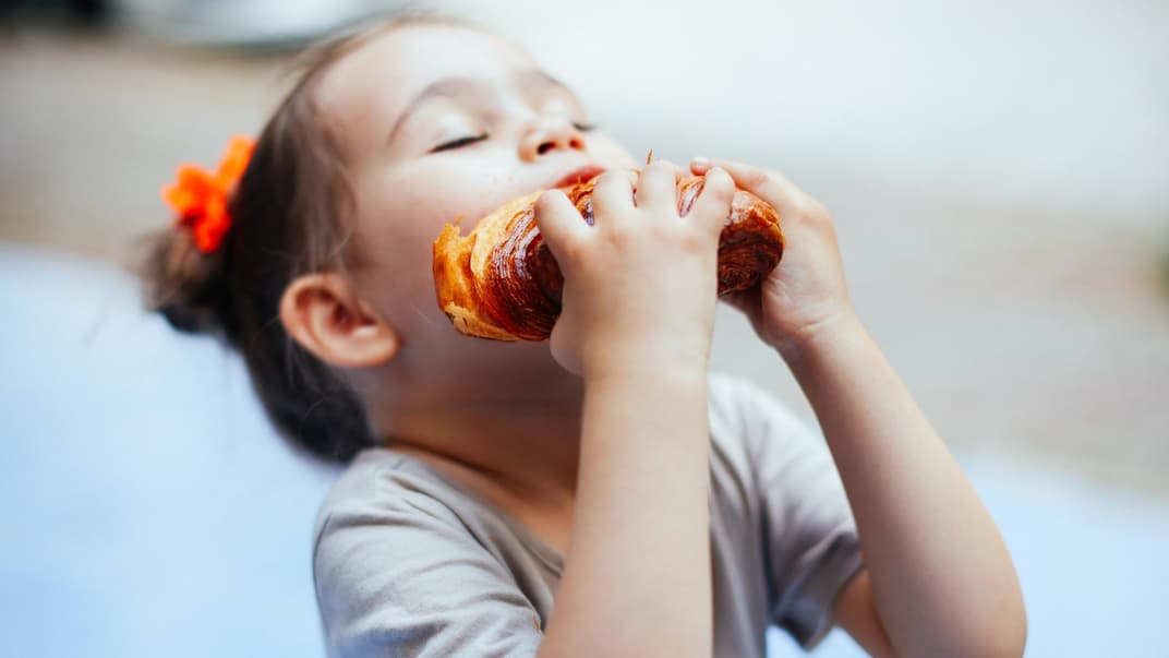 Ein Mädchen beißt in ein Croissant.