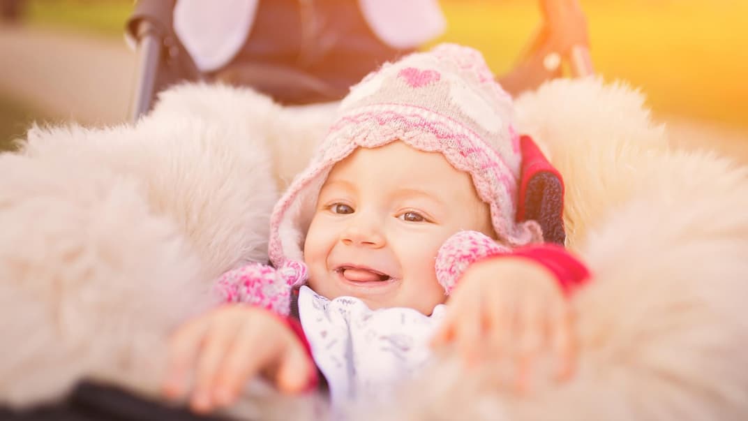 Lachendes Baby in Lammfell-Fußsack im Kinderwagen.