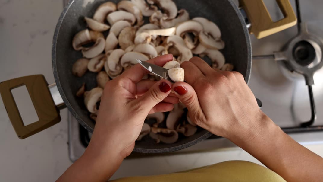 Frau schneidet Champignons in eine Pfanne.