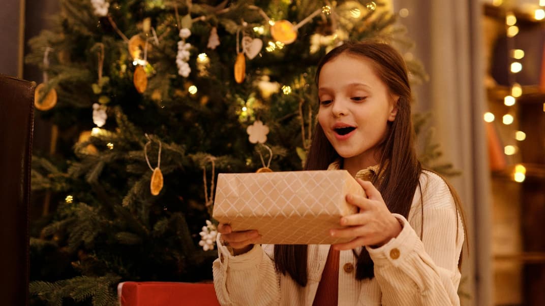 Ein Mädchen sitzt vor em Weihnachtsbaum und freut sich über ihr Geschenk.