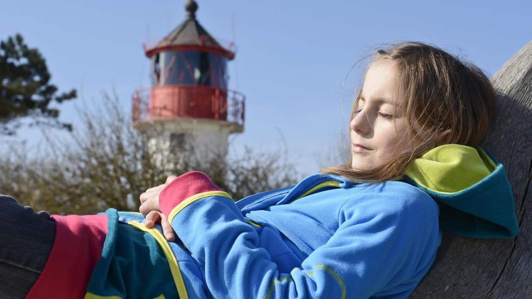 Mädchen chillt vor einem Leuchtturm. 
