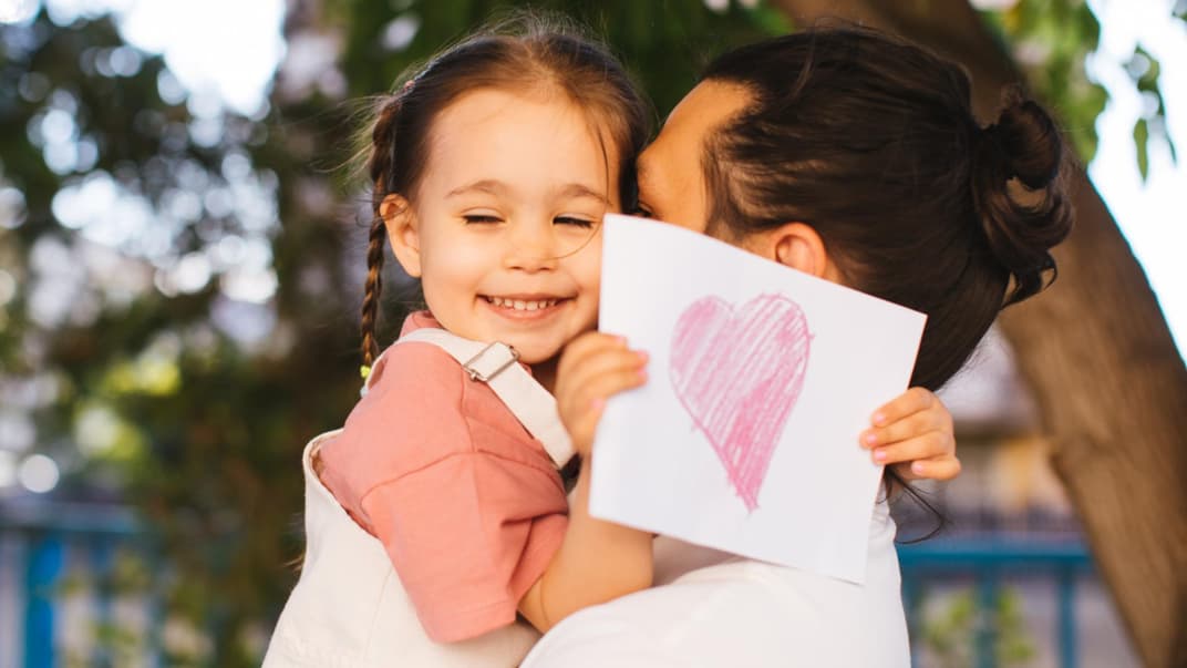 Ein Mädchen mit einer Postkarte in der Hand auf dem Arm ihres Vaters. 