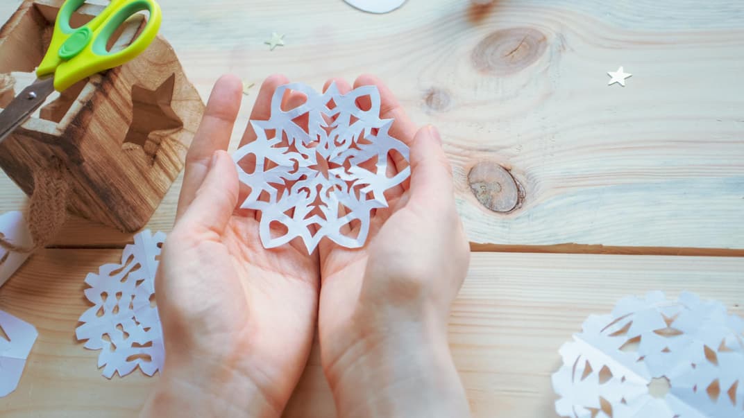 Kind hält selbst gebastelte Schneeflocke in der Hand.