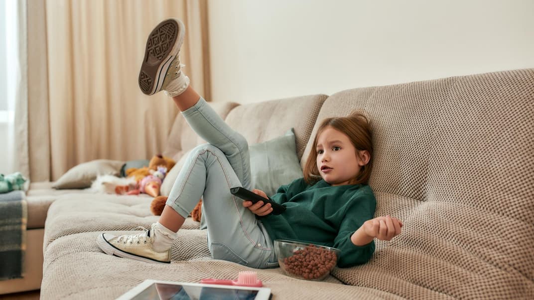 Mädchen auf dem Sofa vorm Fernseher.