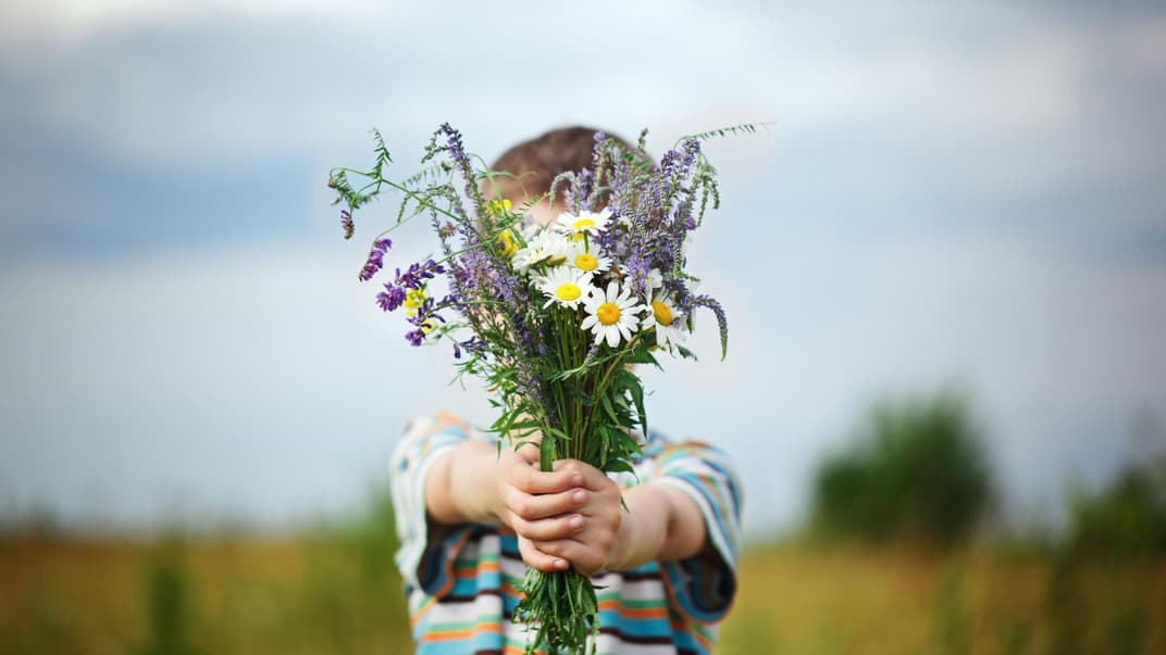 Junge hält Blumenstrauß in die Kamera.