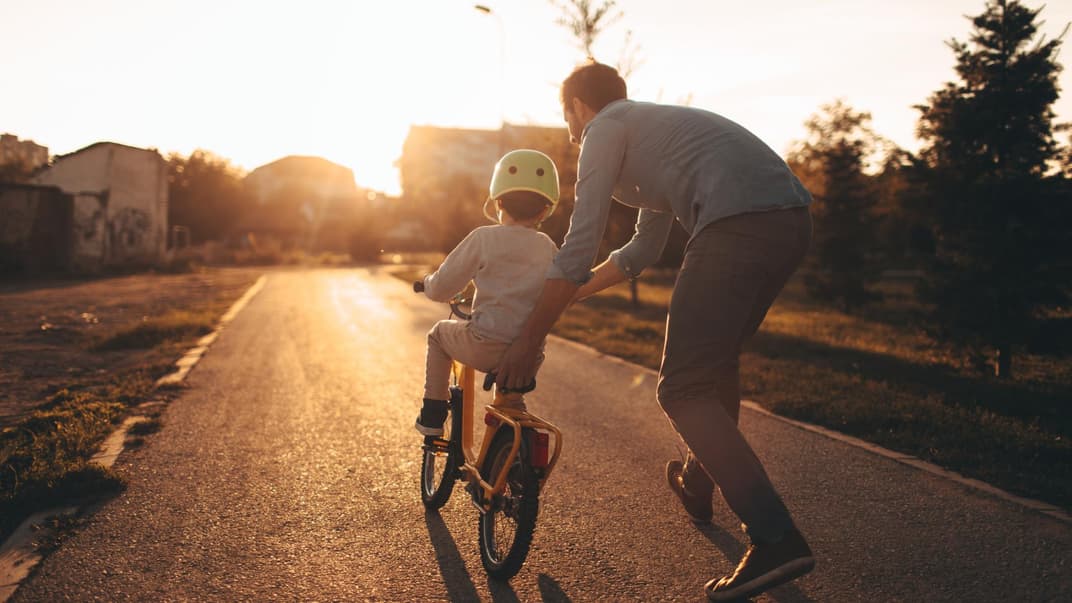 Vater hilft Kind beim Fahrradfahren lernen.
