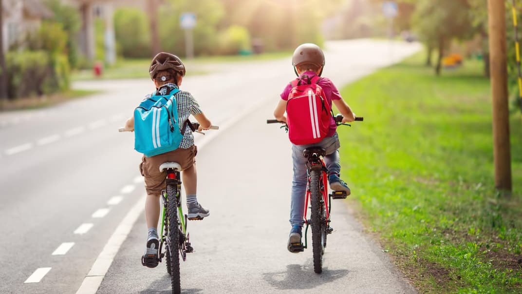Zwei Schulkinder fahren nebeneinander Fahrrad.