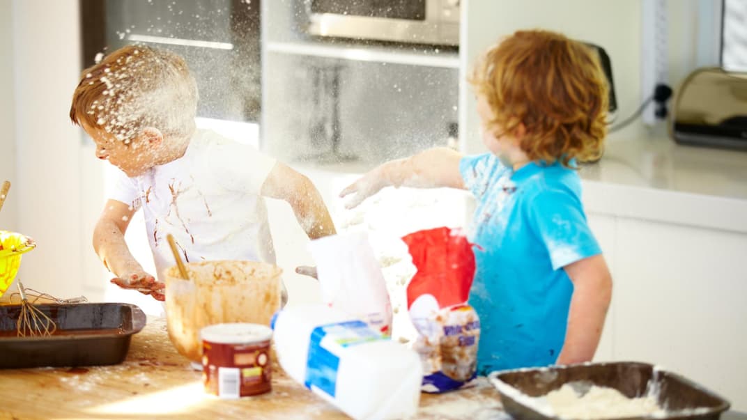 Zwei Kinder streiten beim Backen und bewerfen sich mit Mehl.