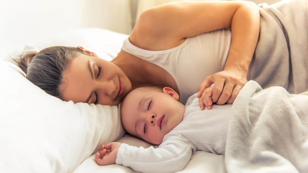 Baby und Mutter schlafen zusammen im Bett.