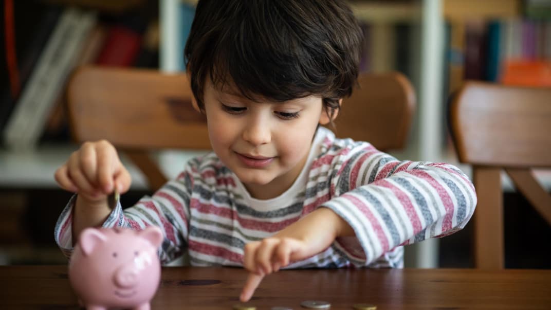 Junge steckt Geld in sein Sparschwein.