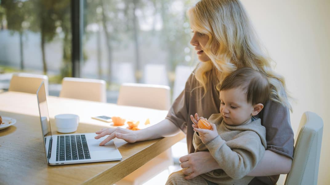 Eine Mutter sitzt am Computer und hat ihren kleinen Sohn auf dem Schoß. 