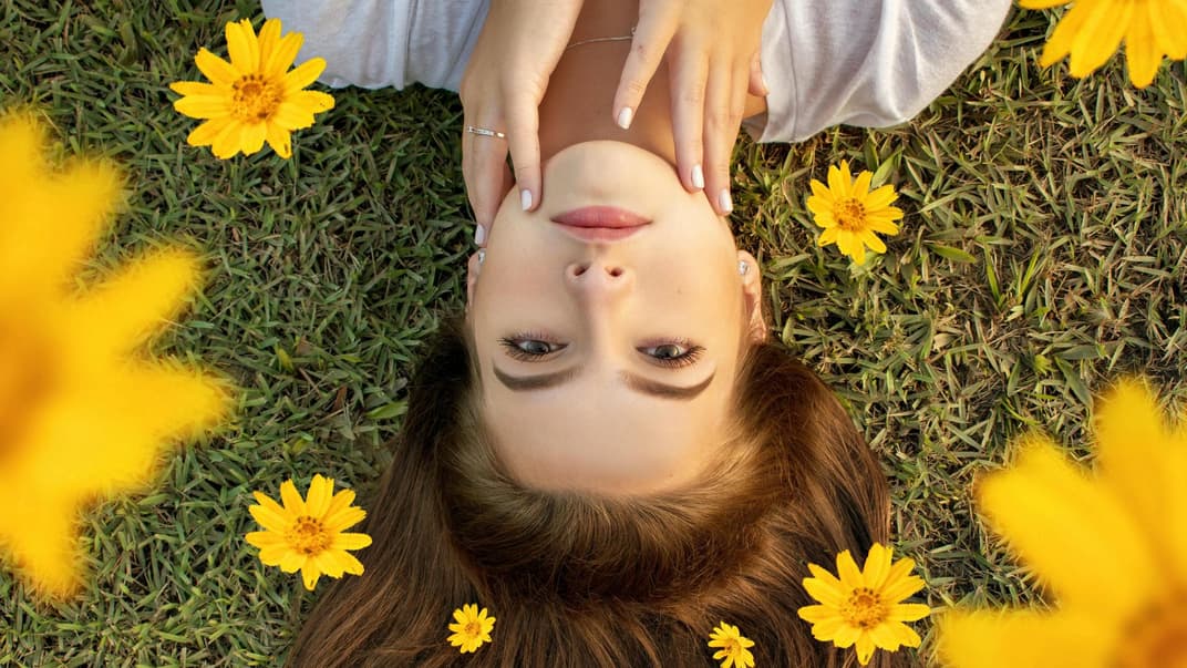 Schöne Frau liegt auf Wiese mit Blüten.