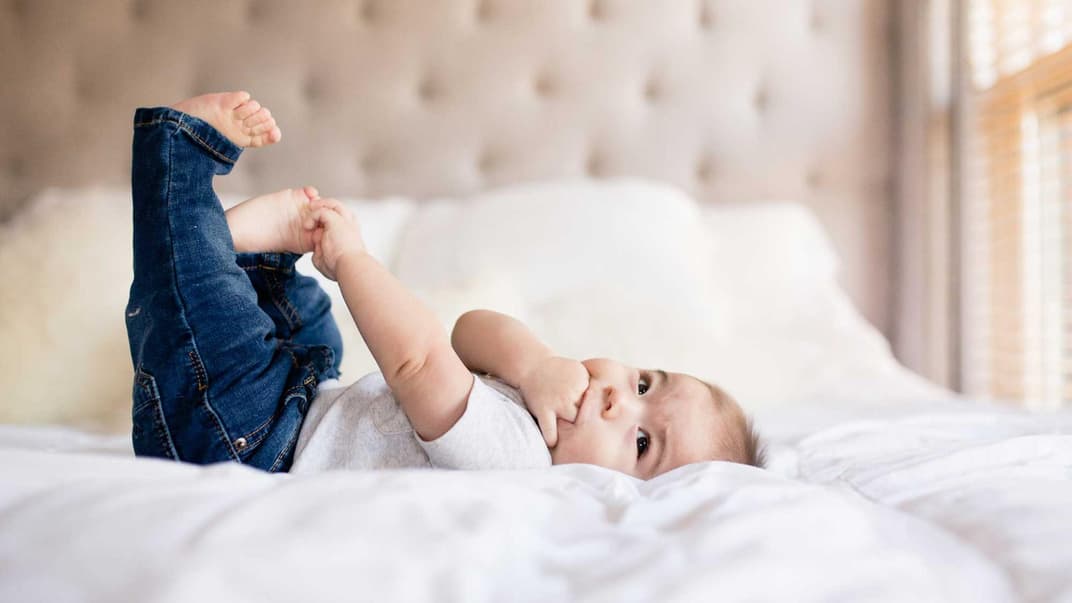 Ein kleines Baby mit Jeans liegt auf einem Bett. 